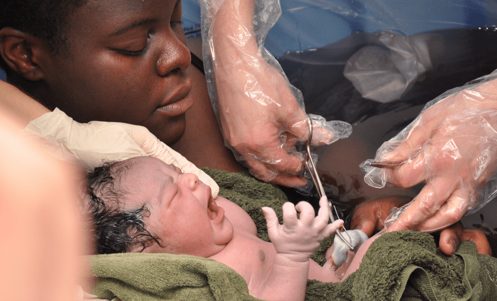 Mother holds newborn as healthcare worker cuts the umbilical cord after a water birth.