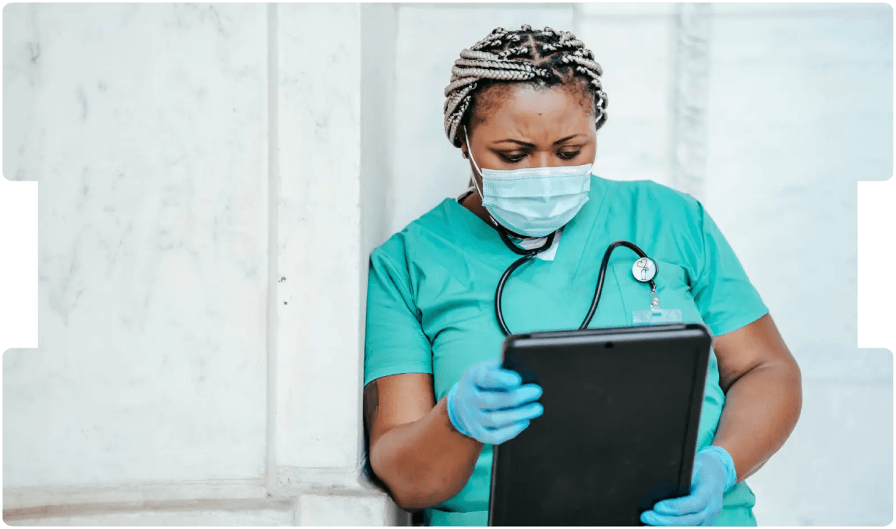 Nurse in scrubs reviewing information on a tablet, reflecting evolving practices and debate over the future of general nursing screening.