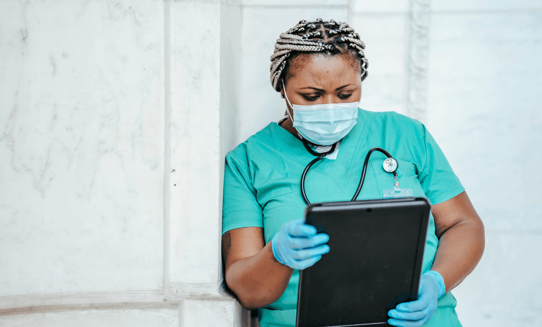 Nurse in scrubs reviewing information on a tablet, reflecting evolving practices and debate over the future of general nursing screening.