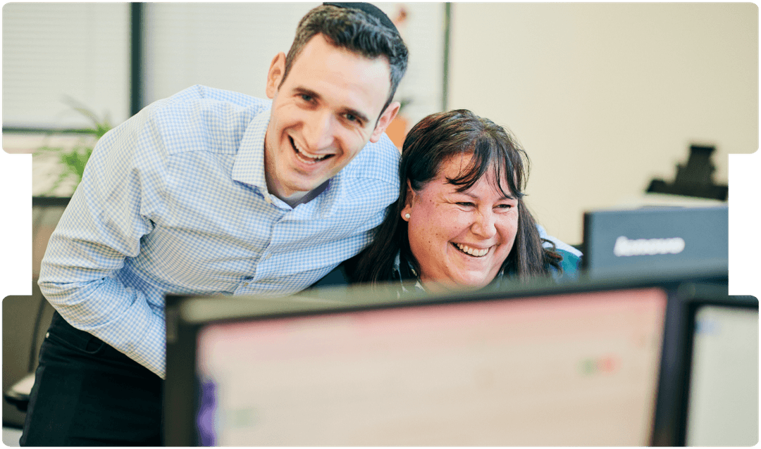 Two colleagues smiling while reviewing feedback on a computer, reflecting teamwork and the value of solicitor feedback in legal case management.