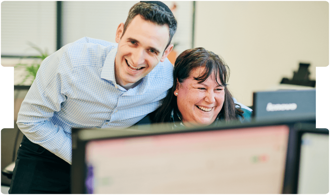 Two colleagues smiling while reviewing feedback on a computer, reflecting teamwork and the value of solicitor feedback in legal case management.