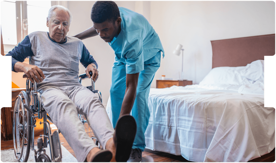 A caregiver helps an elderly man transfer from a wheelchair at home, showing compassionate elderly care, mobility assistance, and professional home care support.