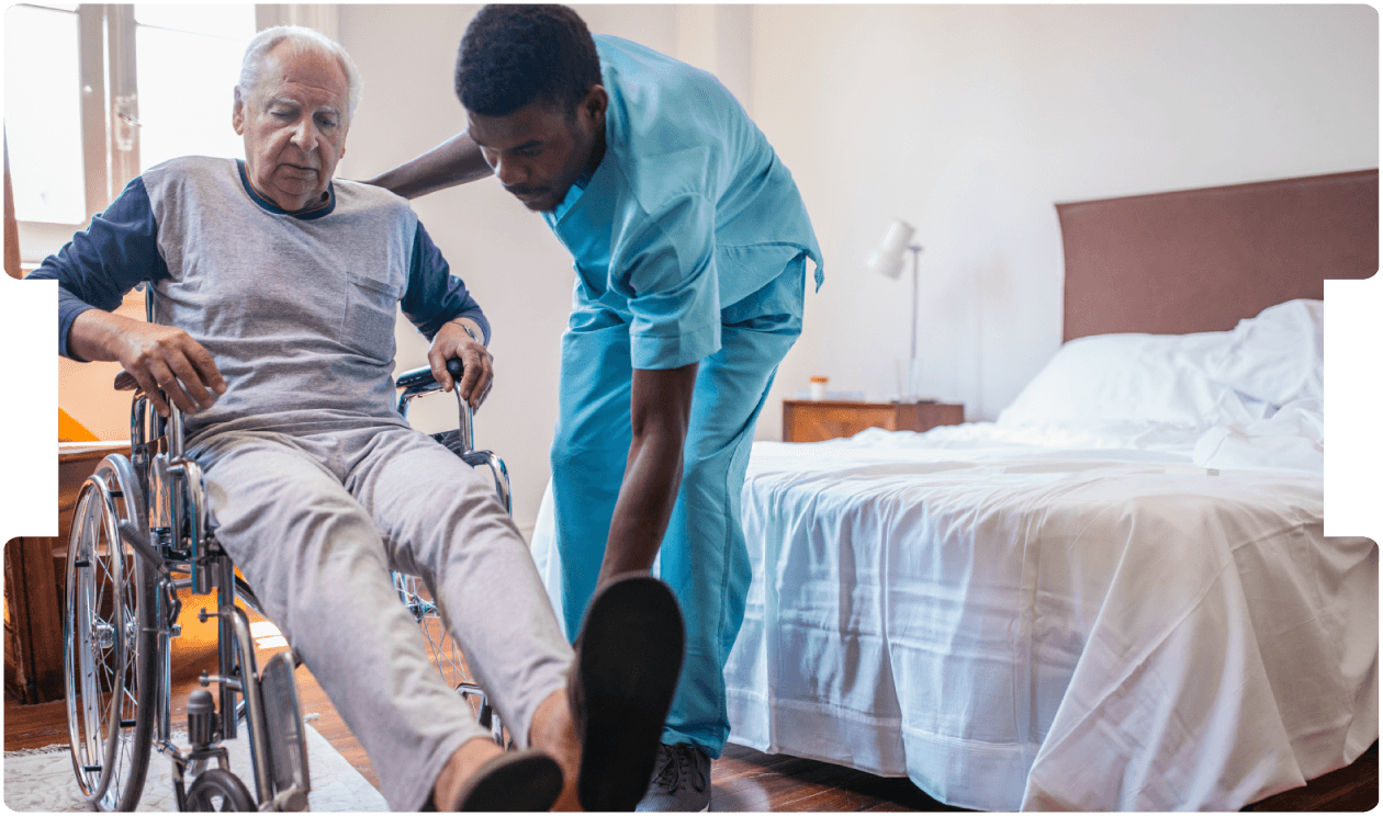 A caregiver helps an elderly man transfer from a wheelchair at home, showing compassionate elderly care, mobility assistance, and professional home care support.