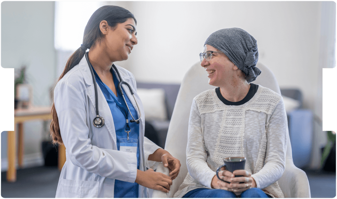 Doctor smiling and talking with a cancer patient wearing a headscarf during a supportive care consultation.