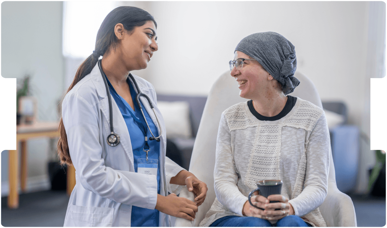 Doctor smiling and talking with a cancer patient wearing a headscarf during a supportive care consultation.