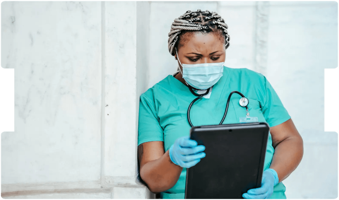 Nurse in scrubs reviewing information on a tablet, reflecting evolving practices and debate over the future of general nursing screening.