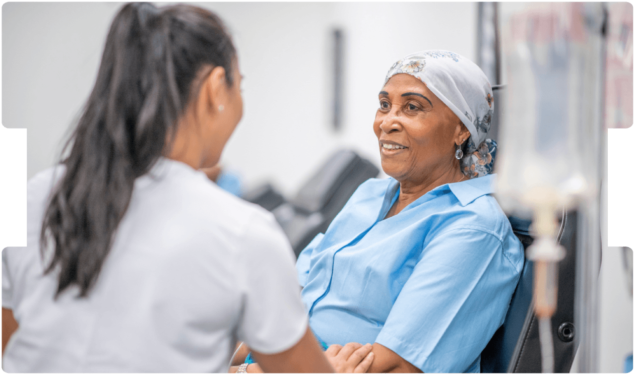 Oncology nurse speaks with a smiling cancer patient during chemotherapy care in a clinic, highlighting compassionate cancer treatment support.