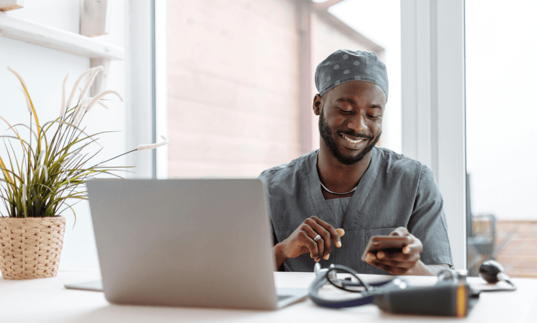 Smiling doctor using a smartphone and laptop, representing the growing role and medico-legal considerations of virtual medical consultations.